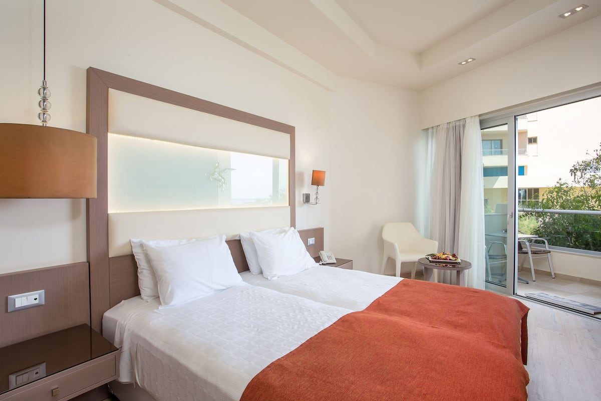 Une chambre d’hôtel avec un grand lit, une table de chevet, une lampe, une chaise et un balcon avec vue.