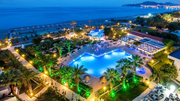 Un resort con una amplia piscina, palmeras y vista al mar.