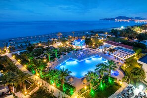 Un resort con una amplia piscina, palmeras y vista al mar.