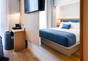 A hotel room with a bed, a desk with a lamp, a TV mounted on the wall, and a window with curtains. - Sanctuary South Beach (MIAMI BEACH)