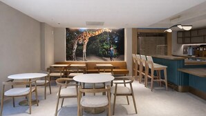 A restaurant with round tables and chairs, a giraffe mural, and a counter with stools. - Sanctuary South Beach (MIAMI BEACH)