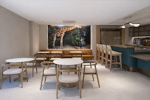 A restaurant with round tables and chairs, a giraffe mural, and a counter with stools. - Sanctuary South Beach (MIAMI BEACH)