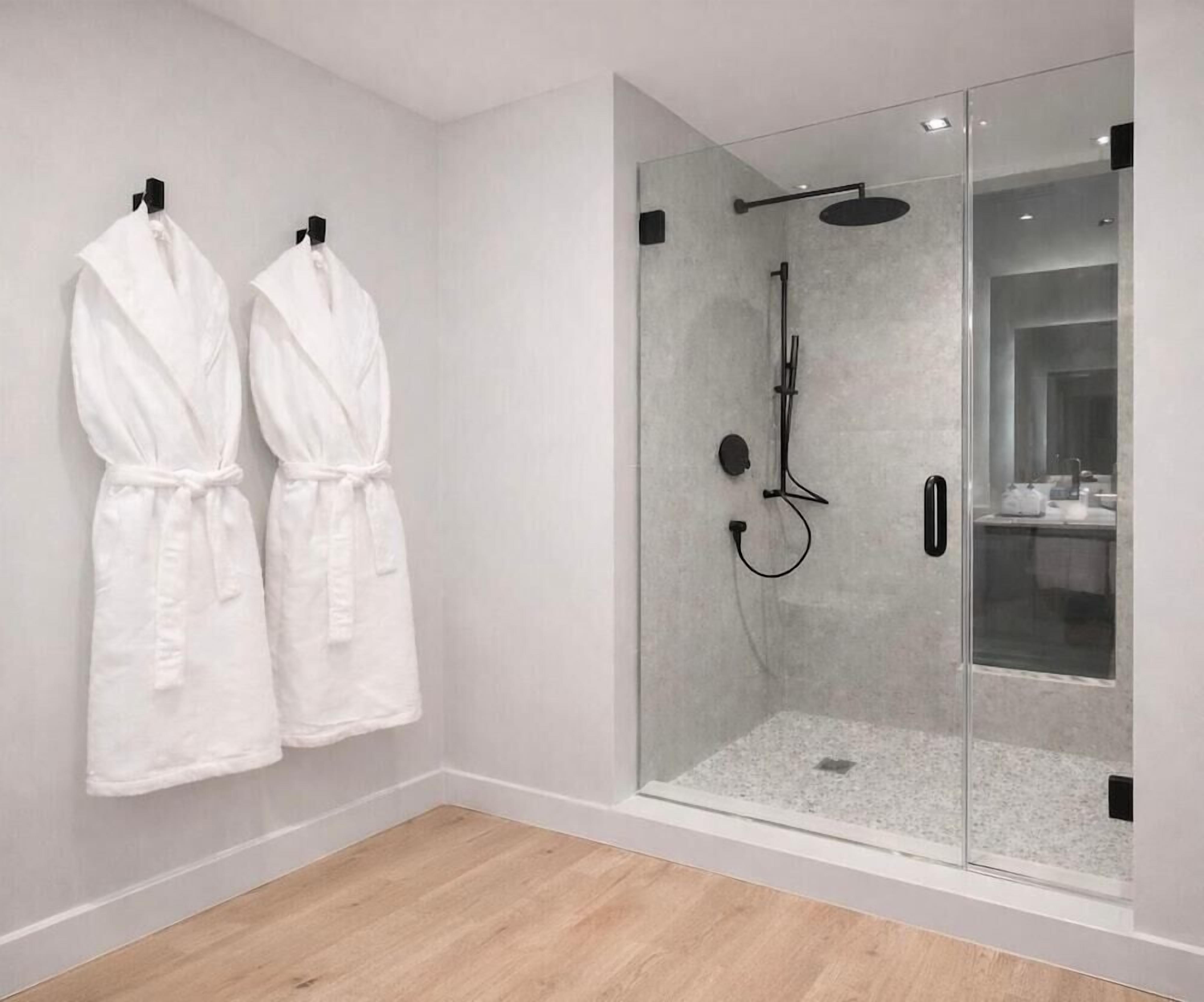 Ein modernes Badezimmer mit einer gläsernen Duschkabine, zwei weißen Handtüchern, die an der Wand hängen, und einem Holzboden.