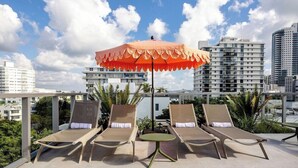 A rooftop lounge area with two sun loungers, a table, and an umbrella. - Sanctuary South Beach (MIAMI BEACH)