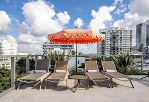 A rooftop lounge area with two sun loungers, a table, and an umbrella. - Sanctuary South Beach (MIAMI BEACH)