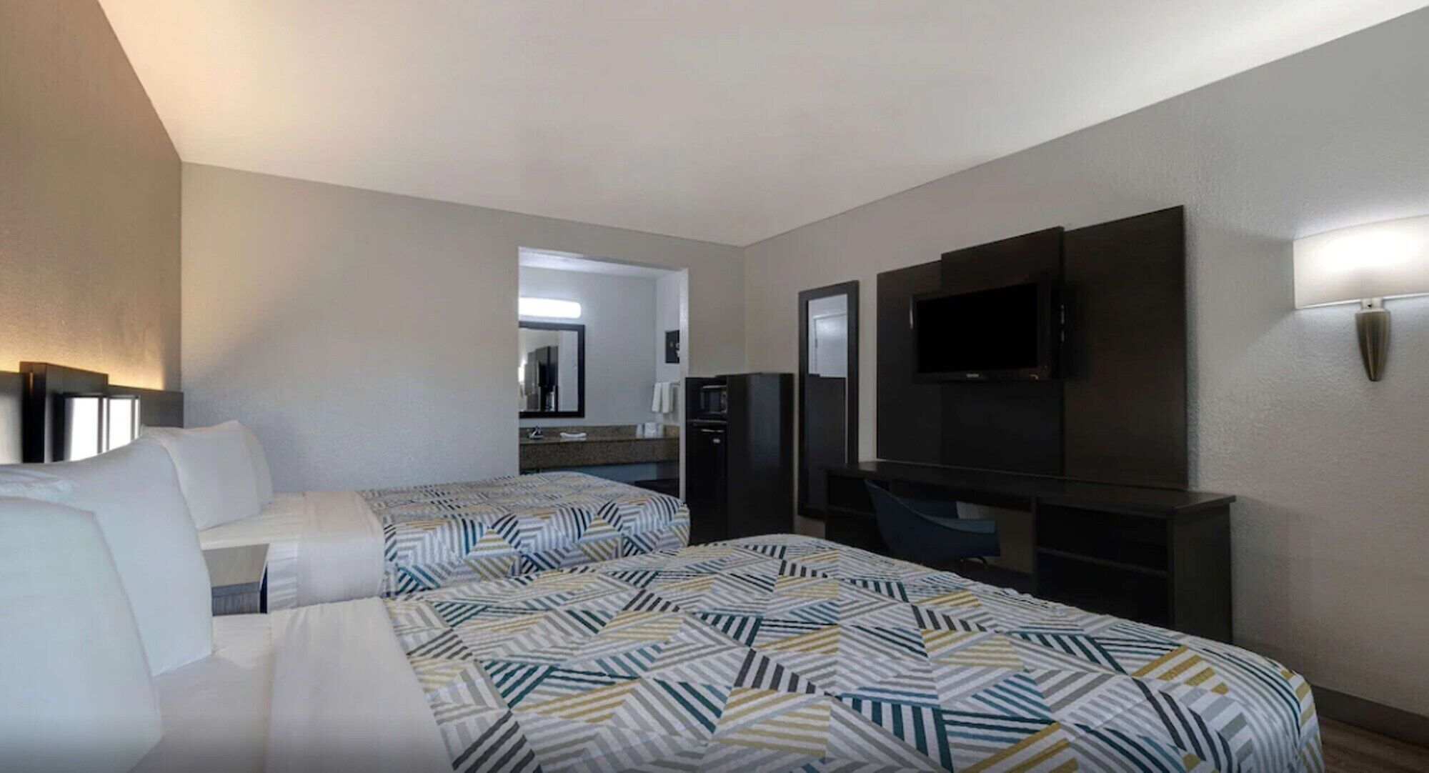 Habitación de hotel con dos camas, televisión, refrigerador y una pequeña kitchenette.