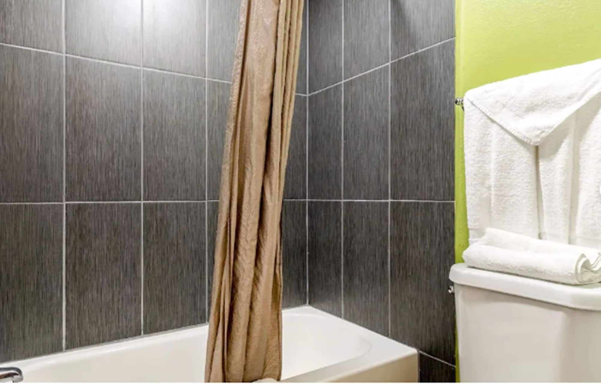 Ein Badezimmer mit dunkelgrauen Fliesen, einer weißen Badewanne und einer grünen Wand.