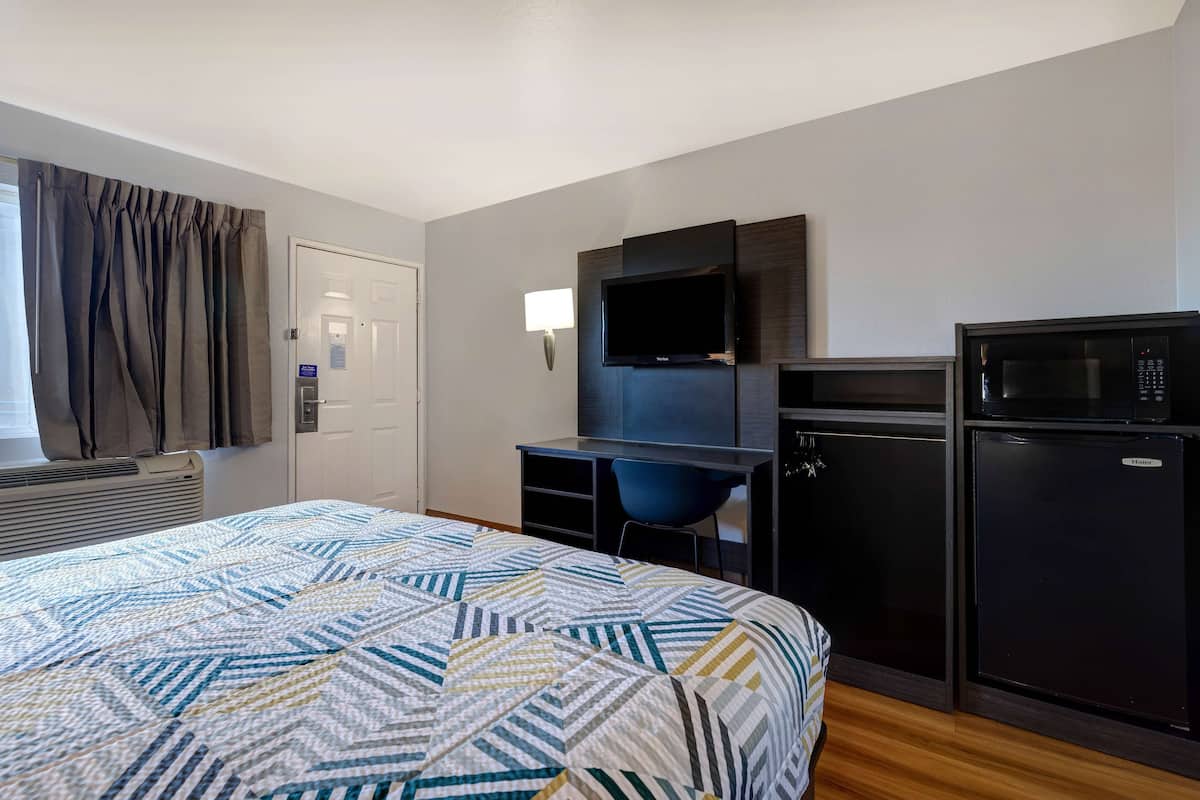 A hotel room with a bed, a desk with a chair, a television, a microwave, and a refrigerator.