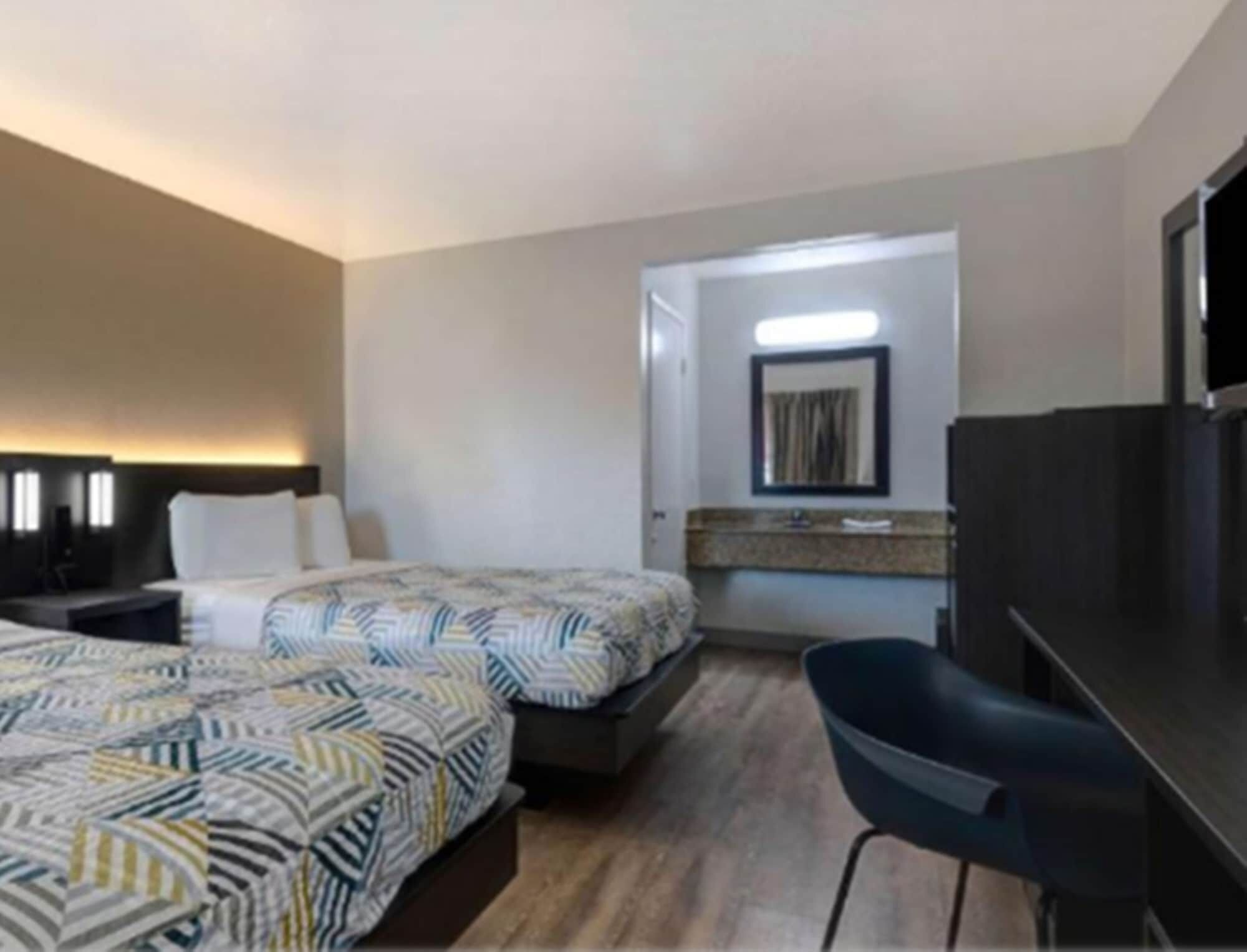 A hotel room with two beds, a desk, a chair, a TV, and a bathroom visible through an open door.