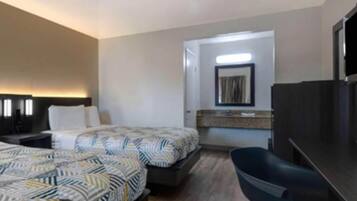 A hotel room with two beds, a desk, a chair, a TV, and a bathroom visible through an open door.