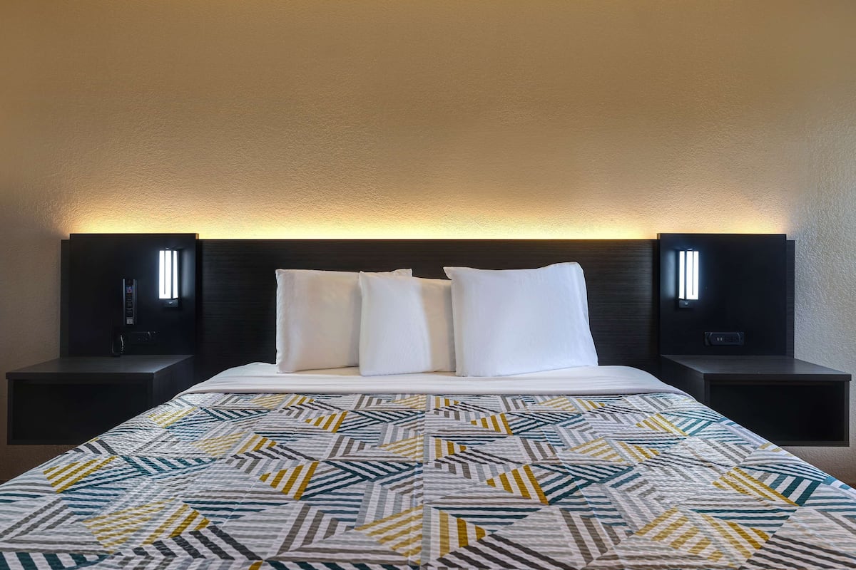 A hotel room with a large bed, two bedside tables, and a headboard with built-in lighting.