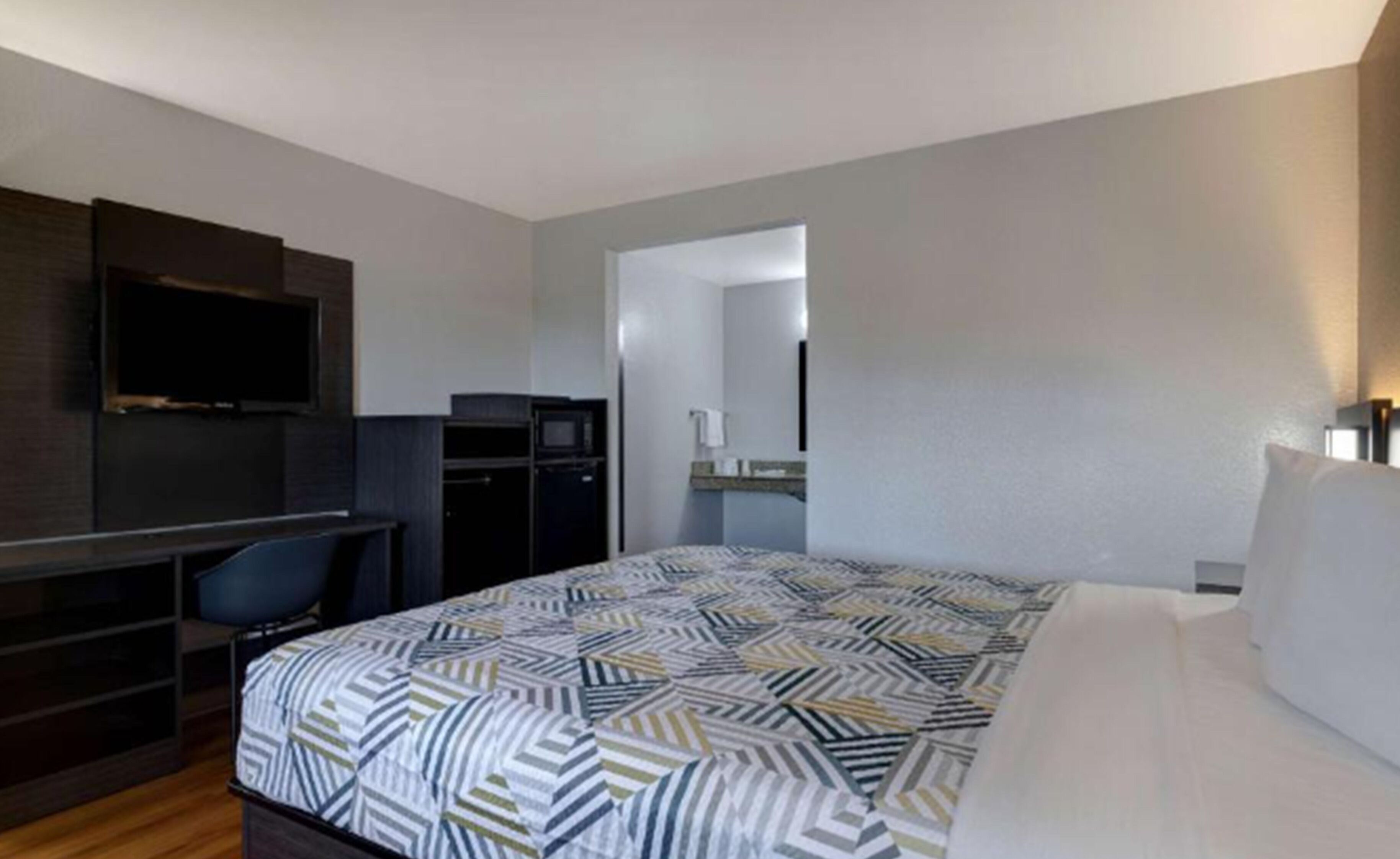 A hotel room with a bed, a desk, a chair, a TV, and a mirror.