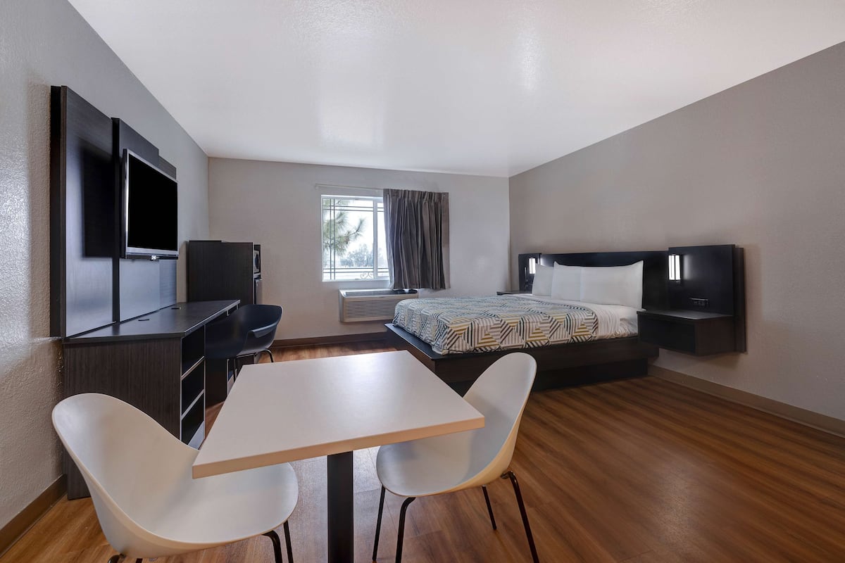 A modern hotel room with a bed, a desk with a chair, a TV, and a window with curtains.