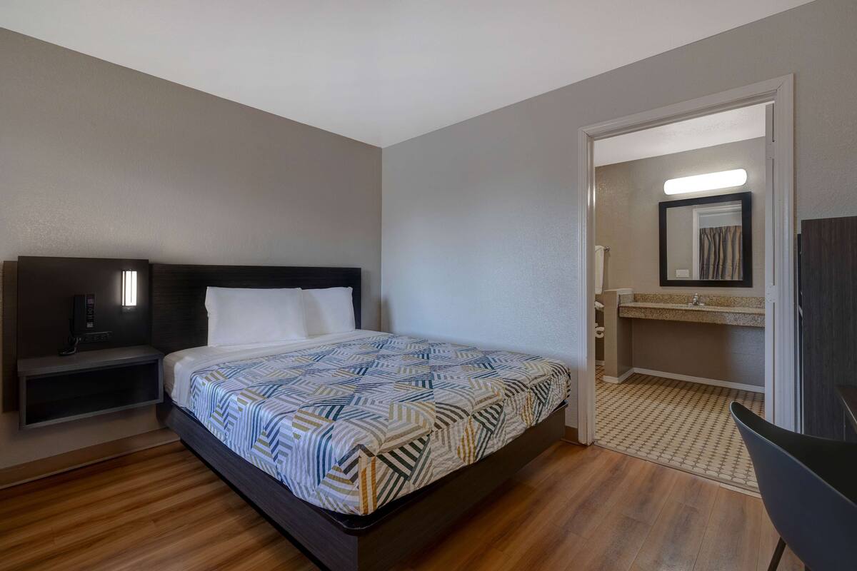A hotel room with a bed, bedside table, and a bathroom visible through an open door.