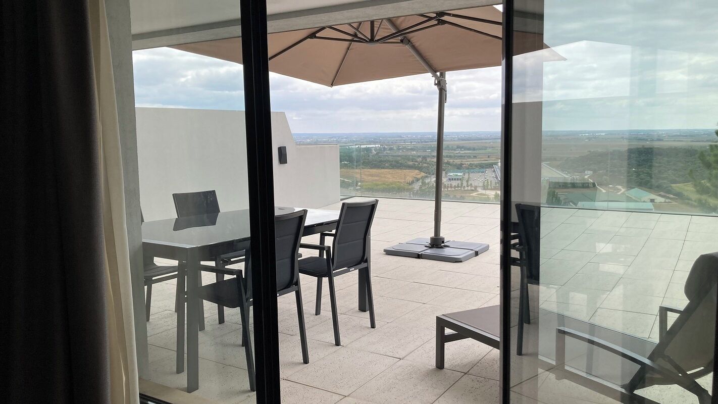 Un balcón con una mesa y sillas de vidrio, una sombrilla y vistas al campo.