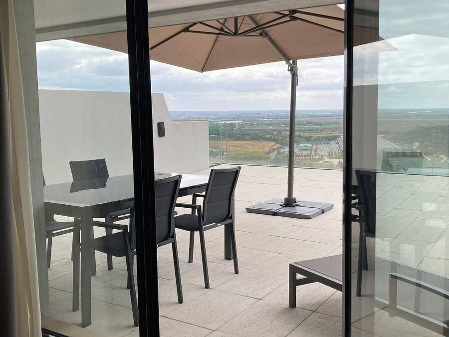 Ein Balkon mit Glastisch und Stühlen, einem Sonnenschirm und Blick auf die Landschaft.