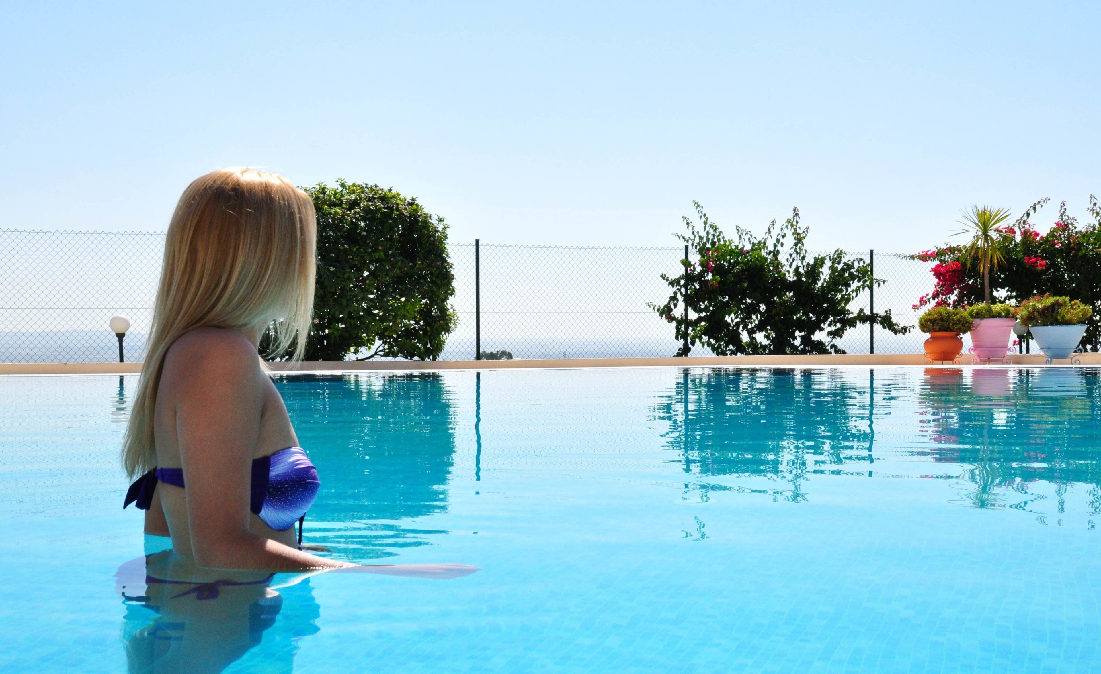 A pool with clear blue water, surrounded by a fence and potted plants.