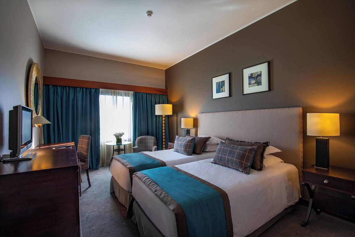 A hotel room with two beds, a desk, a chair, and a small table.