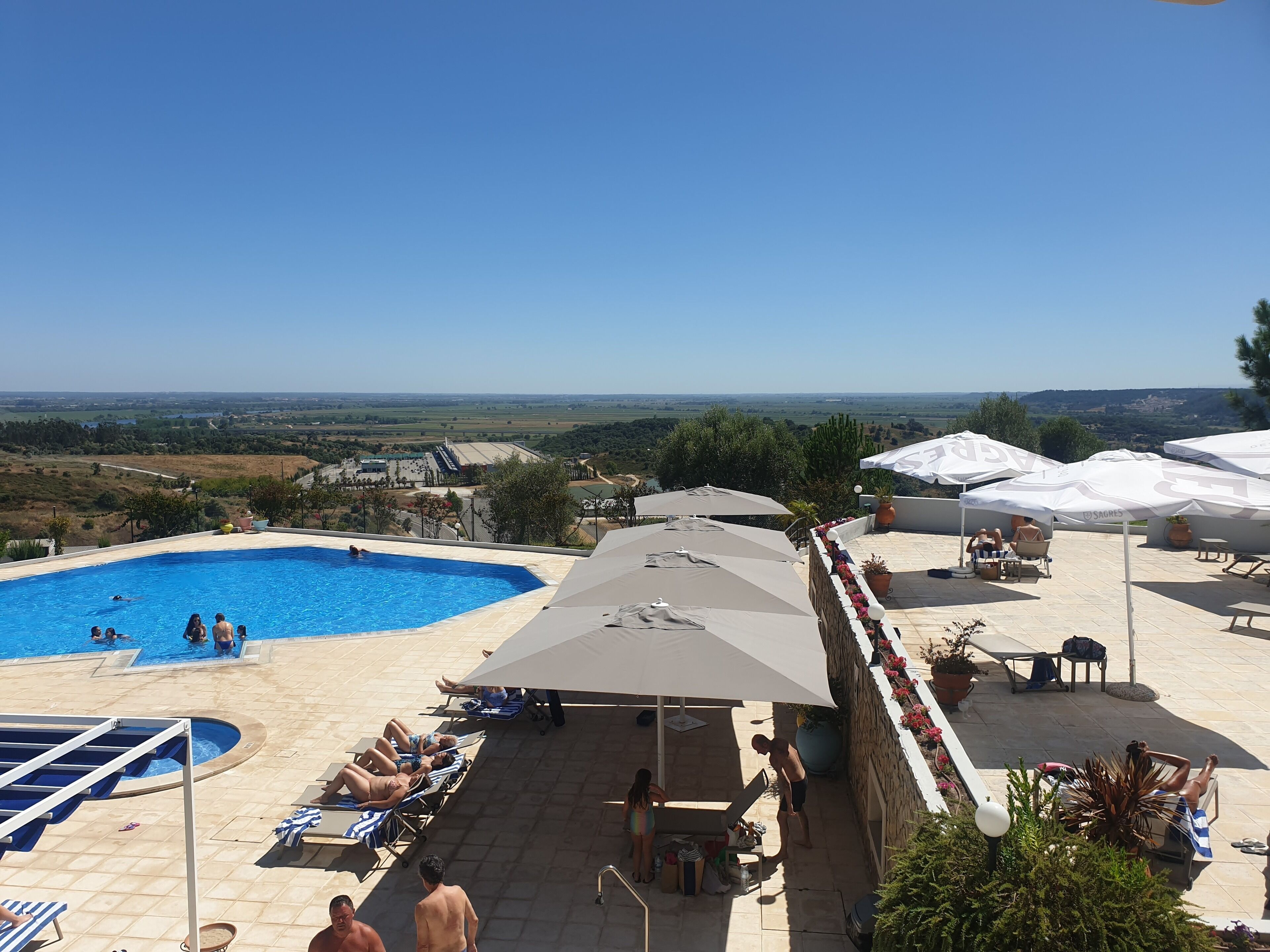 A pool area with multiple sun loungers and umbrellas, a small pool, and a view of the countryside.