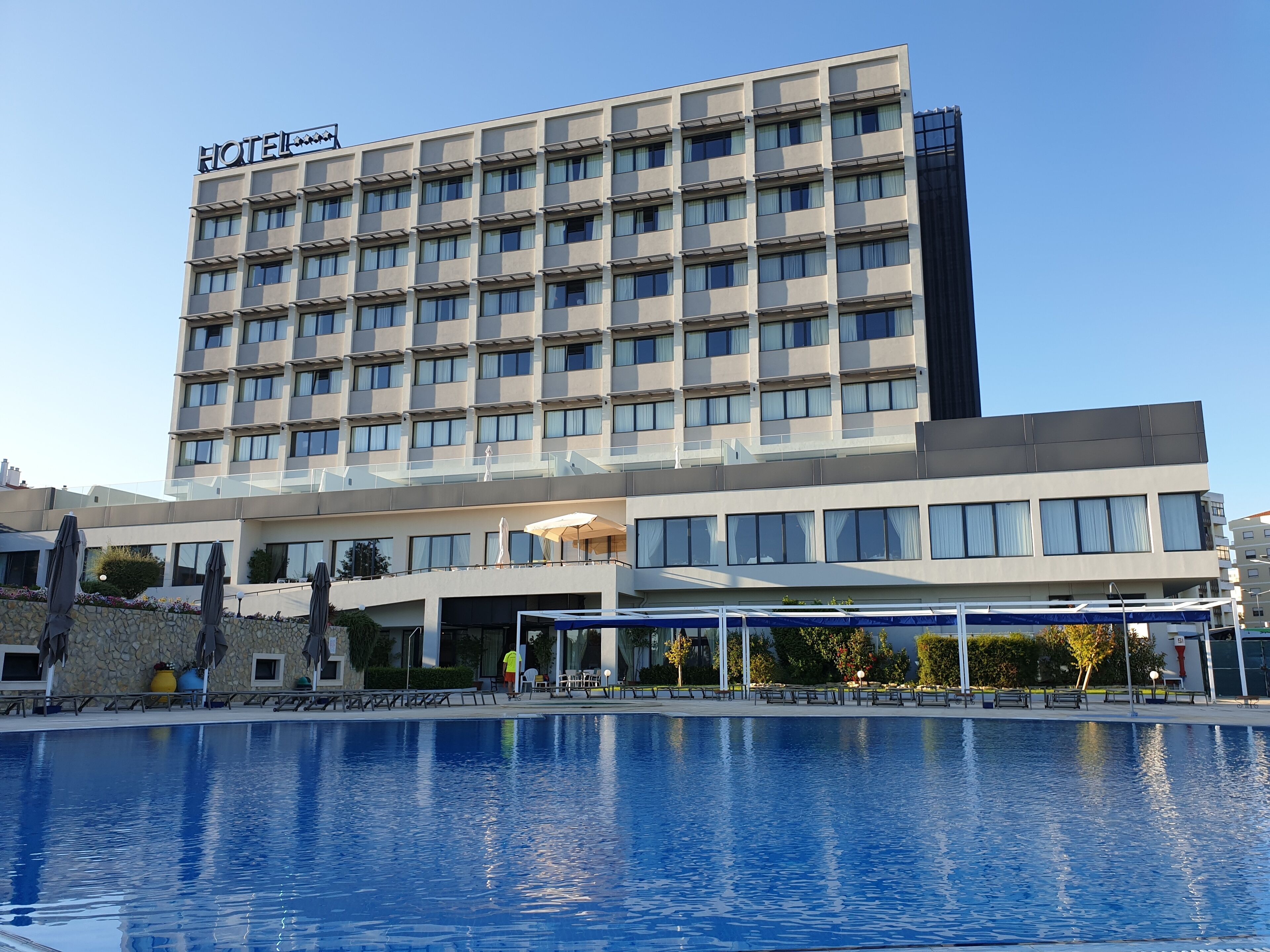 A hotel with a pool, multiple floors, and a clear sky.