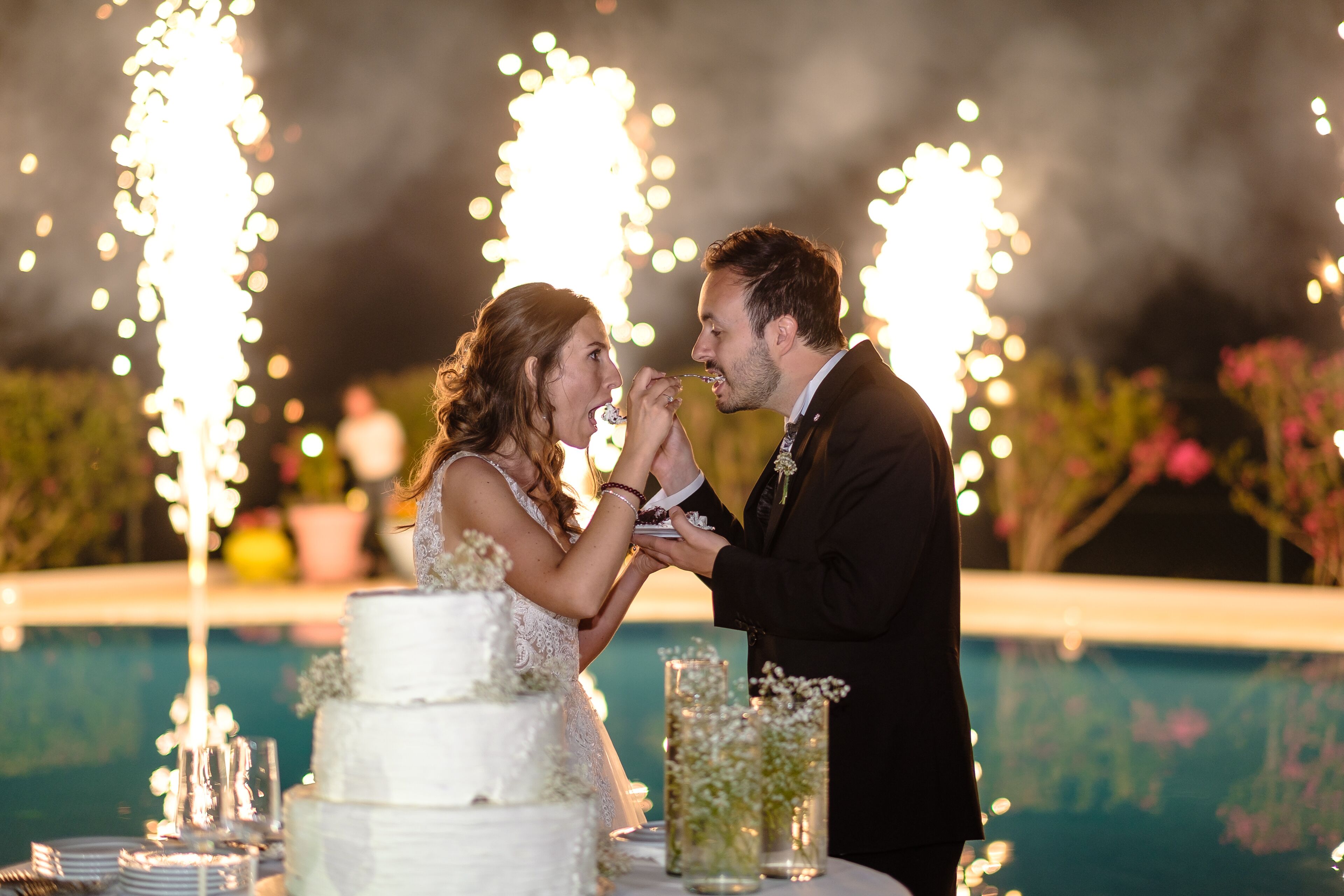 A wedding ceremony with a white cake and sparklers in the background.