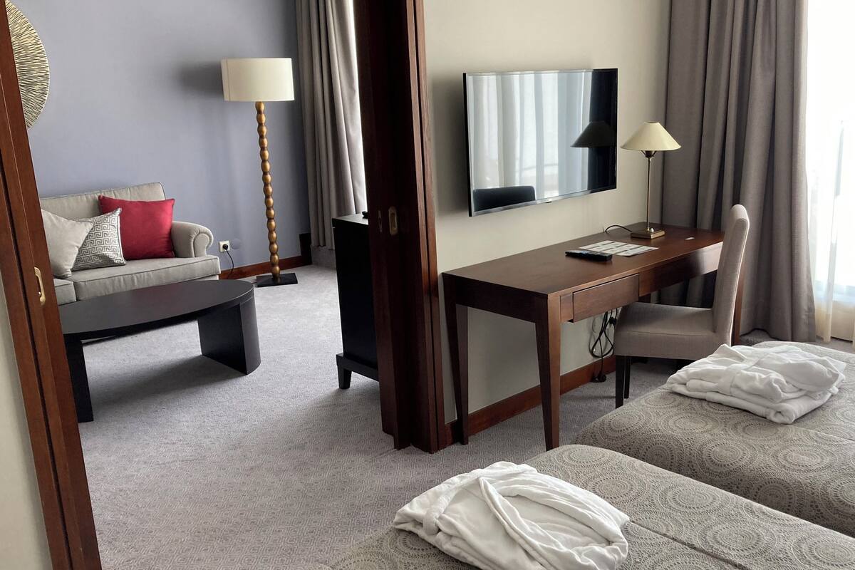 A hotel room with a sofa, a desk, a TV, and a bed with robes.