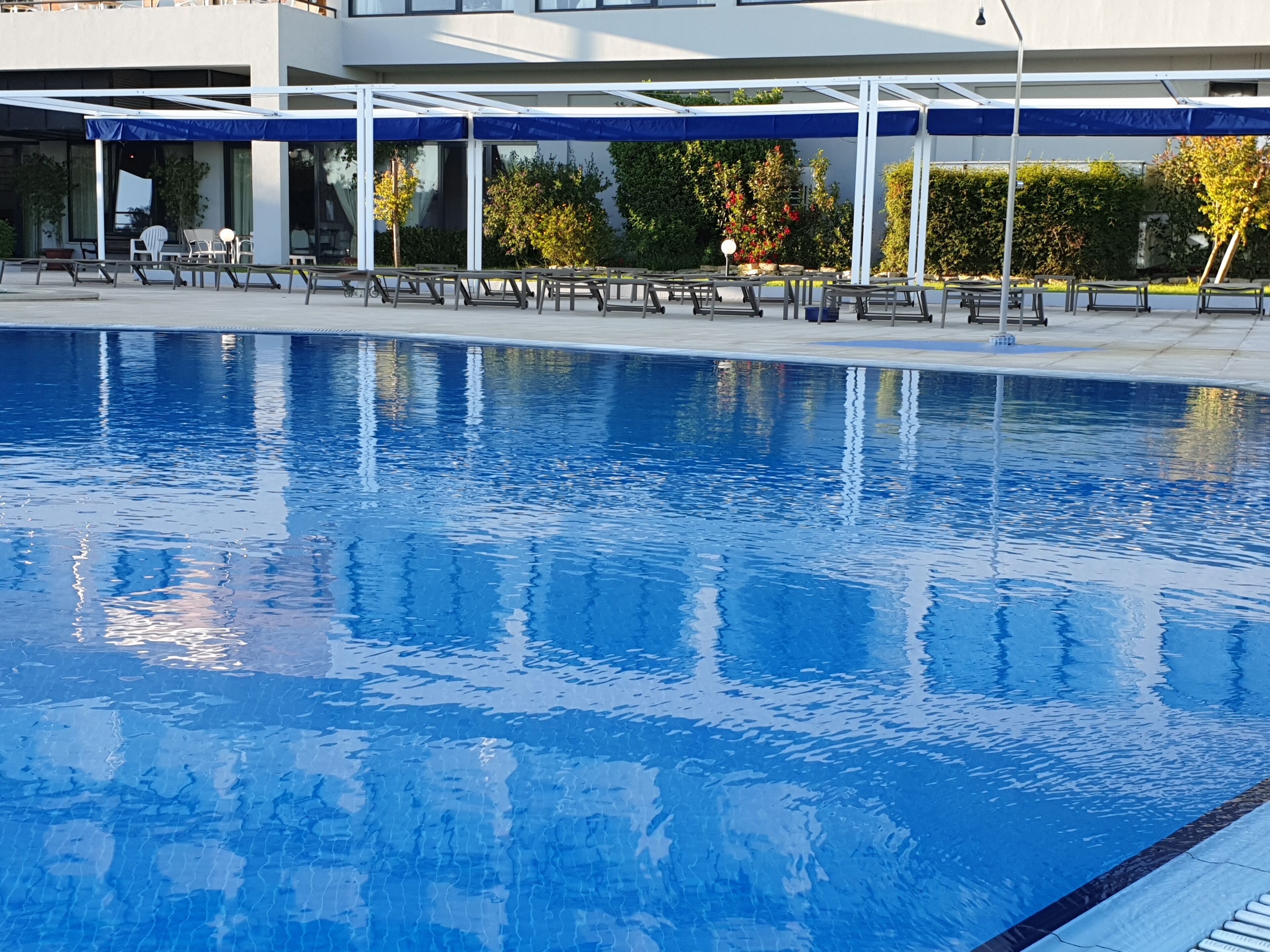 A swimming pool with lounge chairs and umbrellas, surrounded by a building with large windows and greenery.