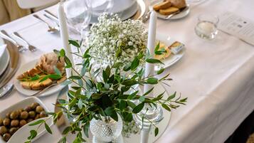 Una mesa dispuesta con platos blancos, cubiertos y un centro de mesa con follaje verde y flores blancas.