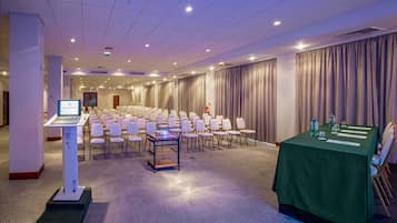 Ein Konferenzraum mit Reihen von Stühlen, einer Projektionsleinwand und einem Tisch mit Wasserflaschen und Gläsern.
