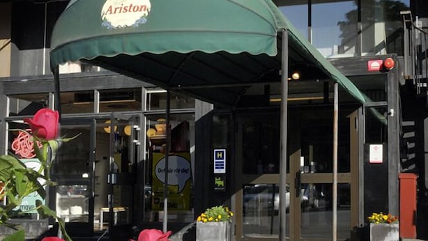 Un restaurant appelé Ariston, avec un auvent vert et des roses rouges en premier plan.