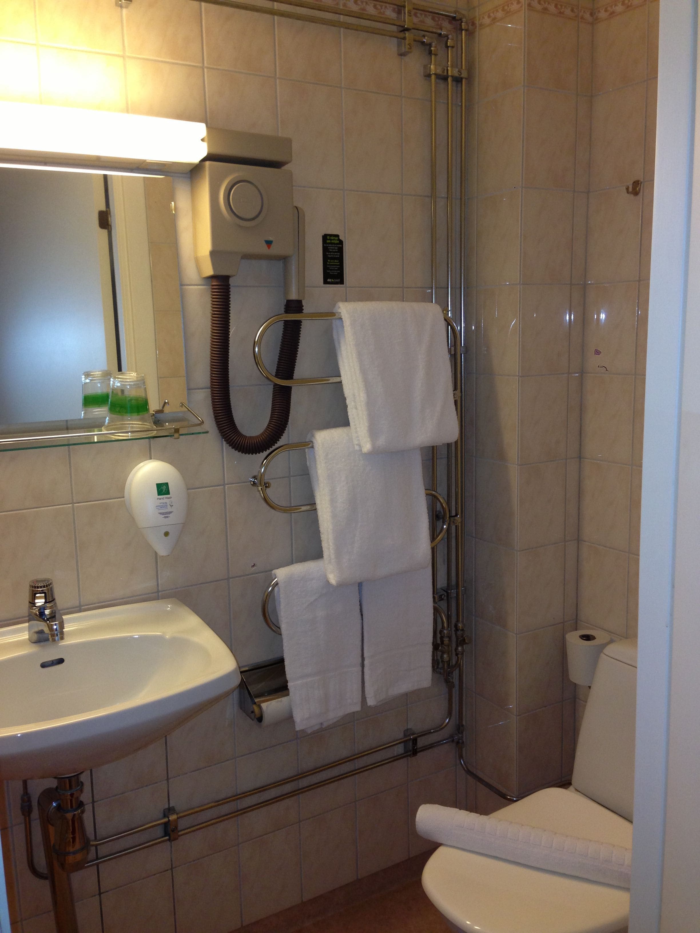 Une salle de bain équipée d’un lavabo, d’un miroir, d’un porte-serviettes, de toilettes et d’un sèche-mains.