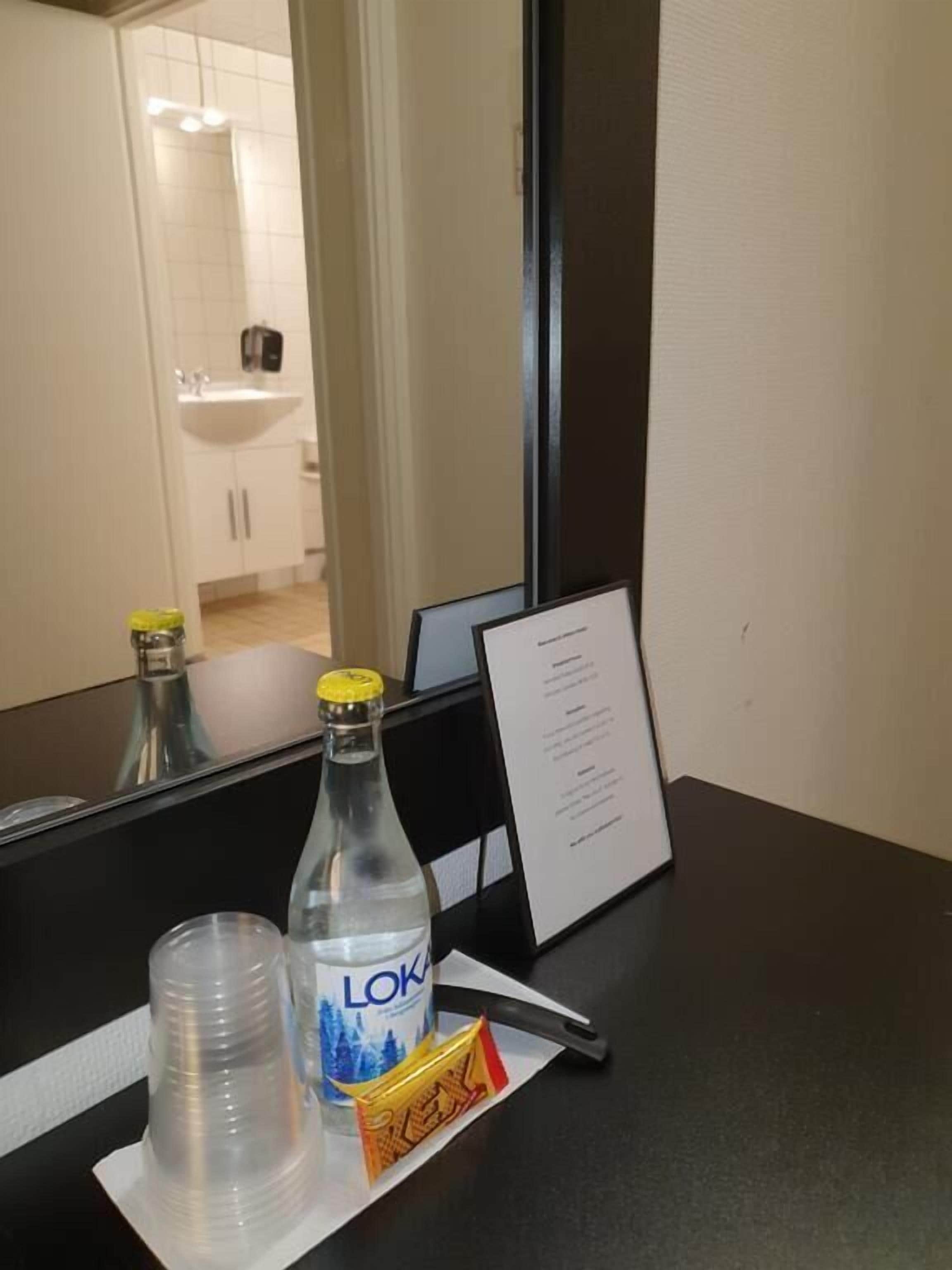 Ein Hotelzimmer mit Spiegel, einer Wasserflasche, einem Plastikbecher und einer Speisekarte auf der Ablagefläche.