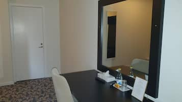 A hotel room with a large mirror, a desk with a chair, a bottle of water, a tissue box, and a sign.