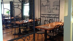Un restaurant avec des tables et des chaises en bois, un paravent décoratif en métal et une fresque murale.