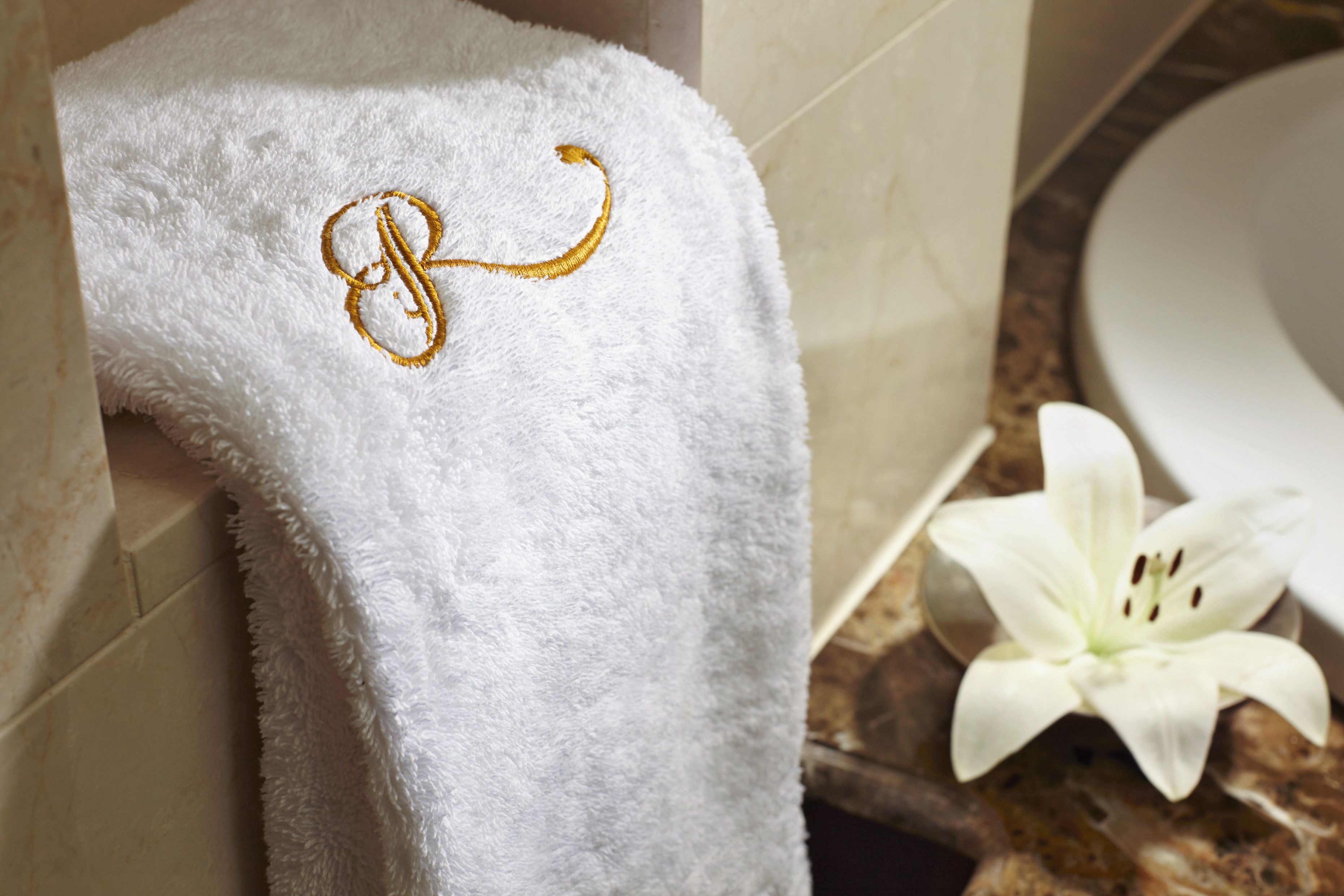 Toalla blanca con un monograma bordado en dorado colgada en una pared de baño.