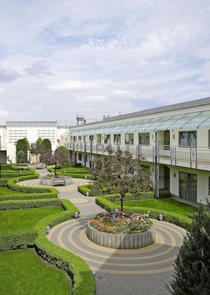 A modern building with a glass-roofed corridor, landscaped gardens, and a central circular flower bed.