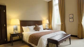 Habitación de hotel con una cama grande, dos mesitas de noche con lámparas, un banco y una ventana con cortinas.