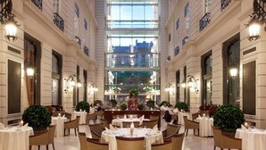 Un amplio comedor con mesas y sillas redondas, ventanas grandes y luminarias decorativas.
