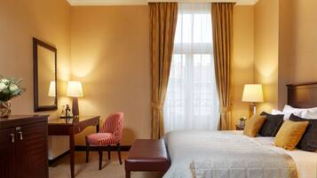 A hotel room with a bed, a desk with a chair, a lamp, and a mirror.