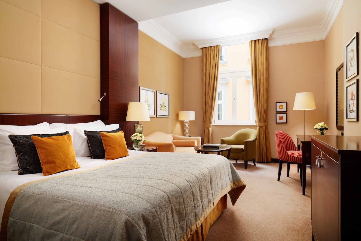 Een hotelkamer met een groot bed, twee fauteuils, een bureau en een raam met gordijnen.