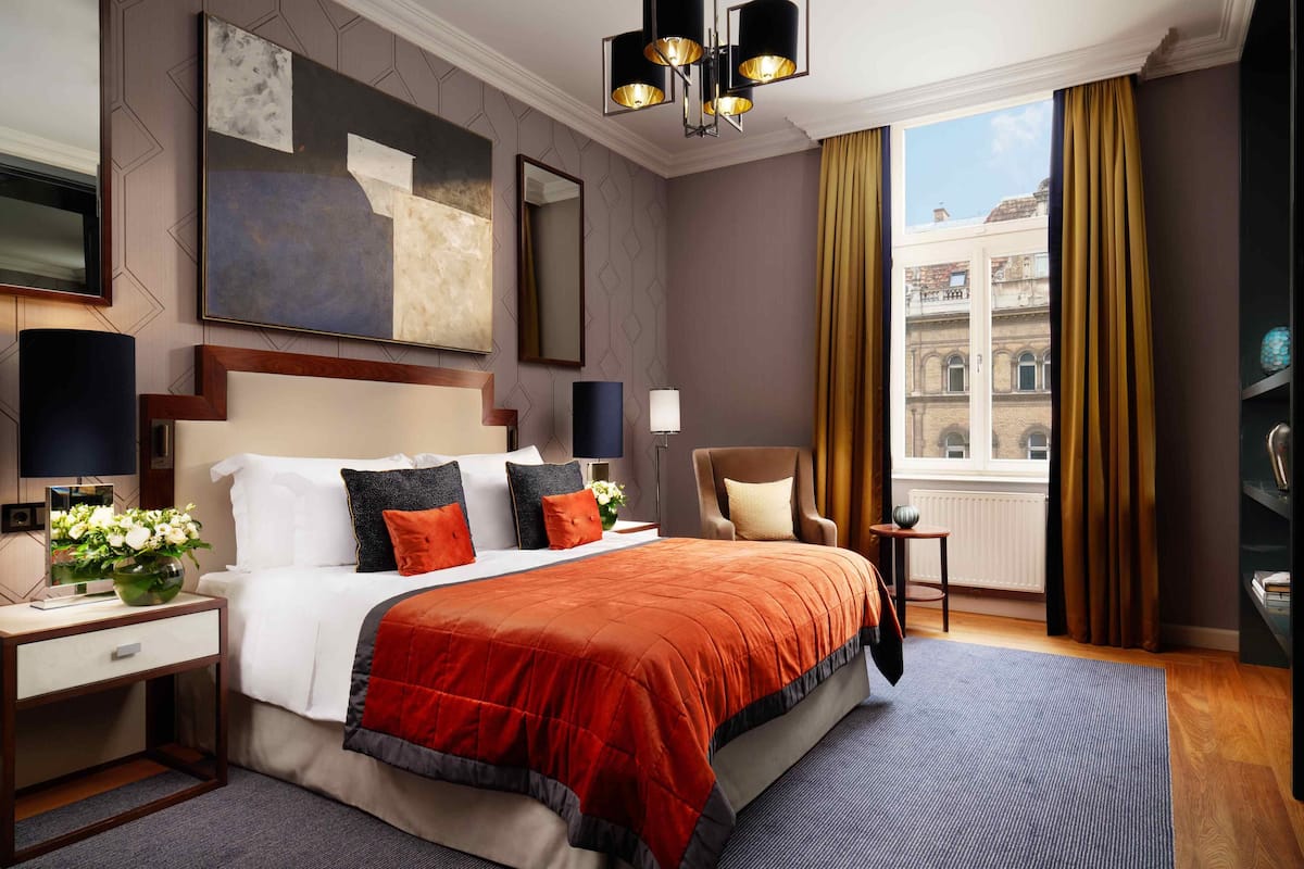 Hotelkamer met een groot bed, een bureau met lamp, een stoel en uitzicht op gebouwen door het raam.