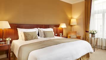 Habitación de hotel con una cama grande, dos mesitas de noche con lámparas, una pequeña mesa con un florero y una ventana con cortinas.
