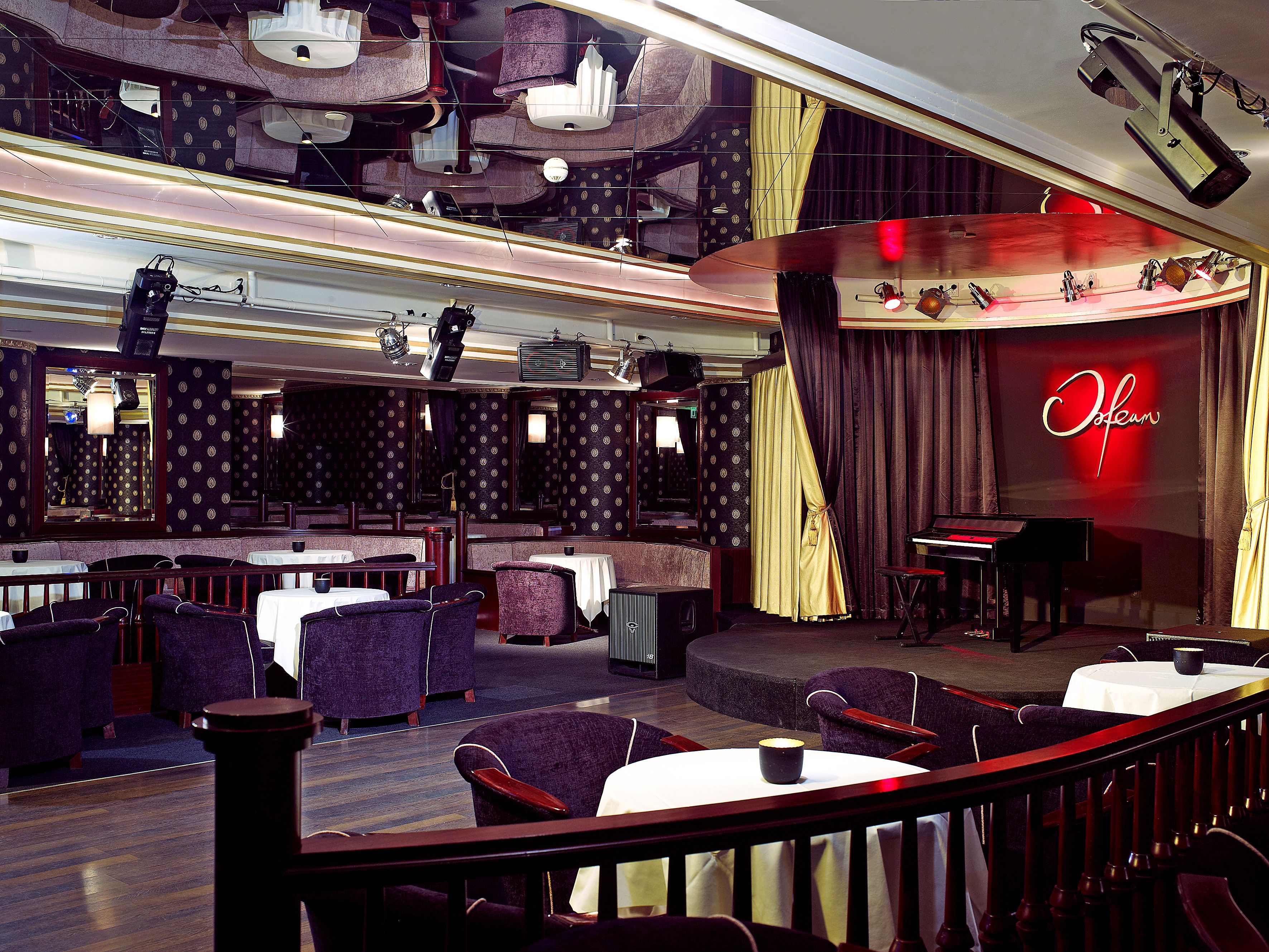 A restaurant with a stage, tables, chairs, and a piano.