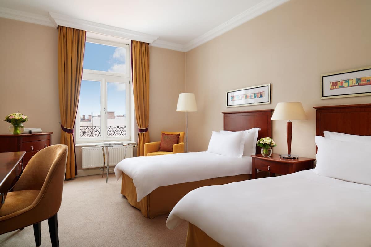 Een hotelkamer met twee bedden, een bureau, een stoel en een raam met gordijnen.