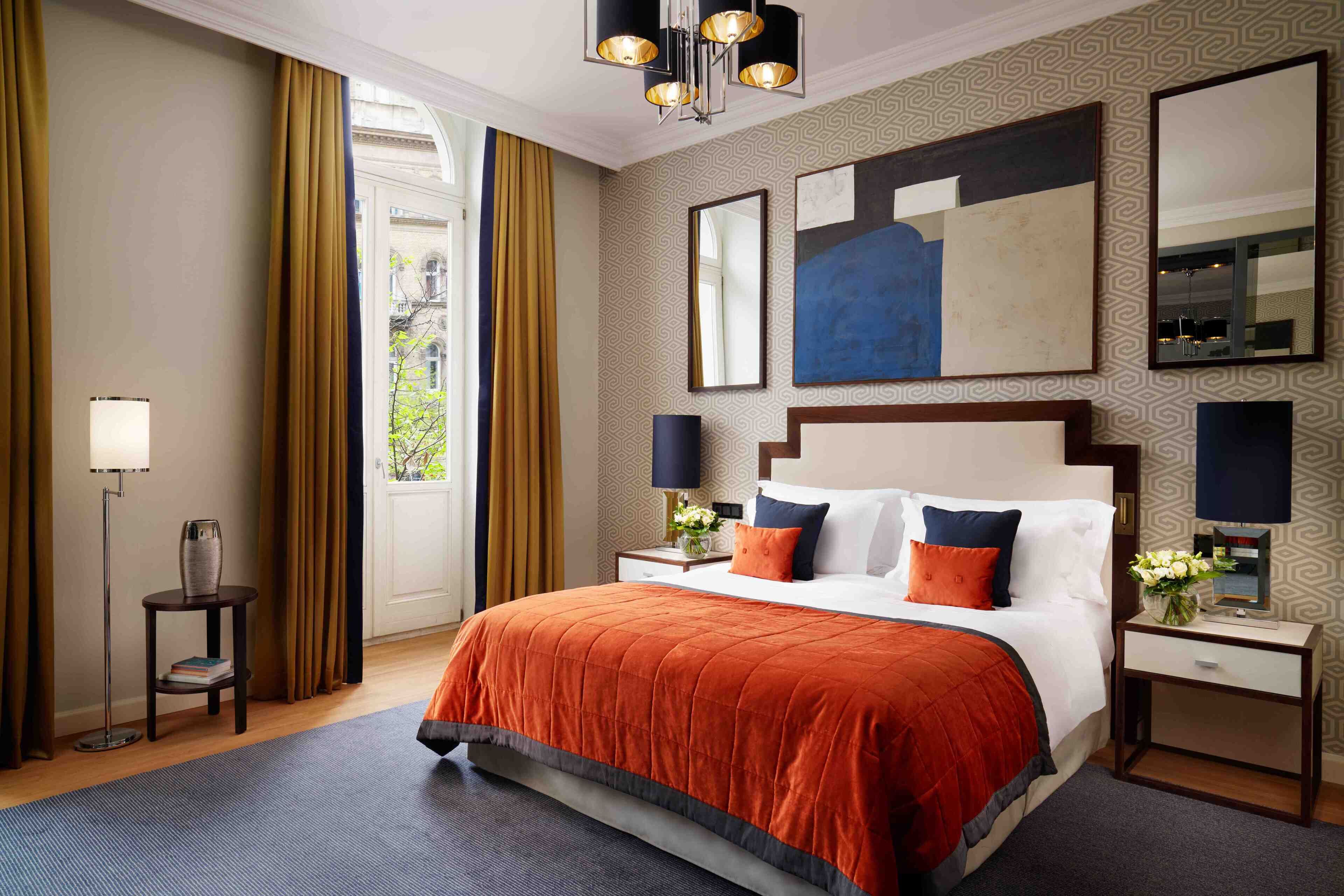 Hotelkamer met een groot bed, twee nachtkastjes, een vloerlamp en een groot raam met gordijnen.