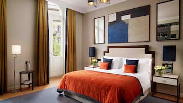 A hotel room with a large bed, two bedside tables, a nightstand, a floor lamp, and a large window with curtains.