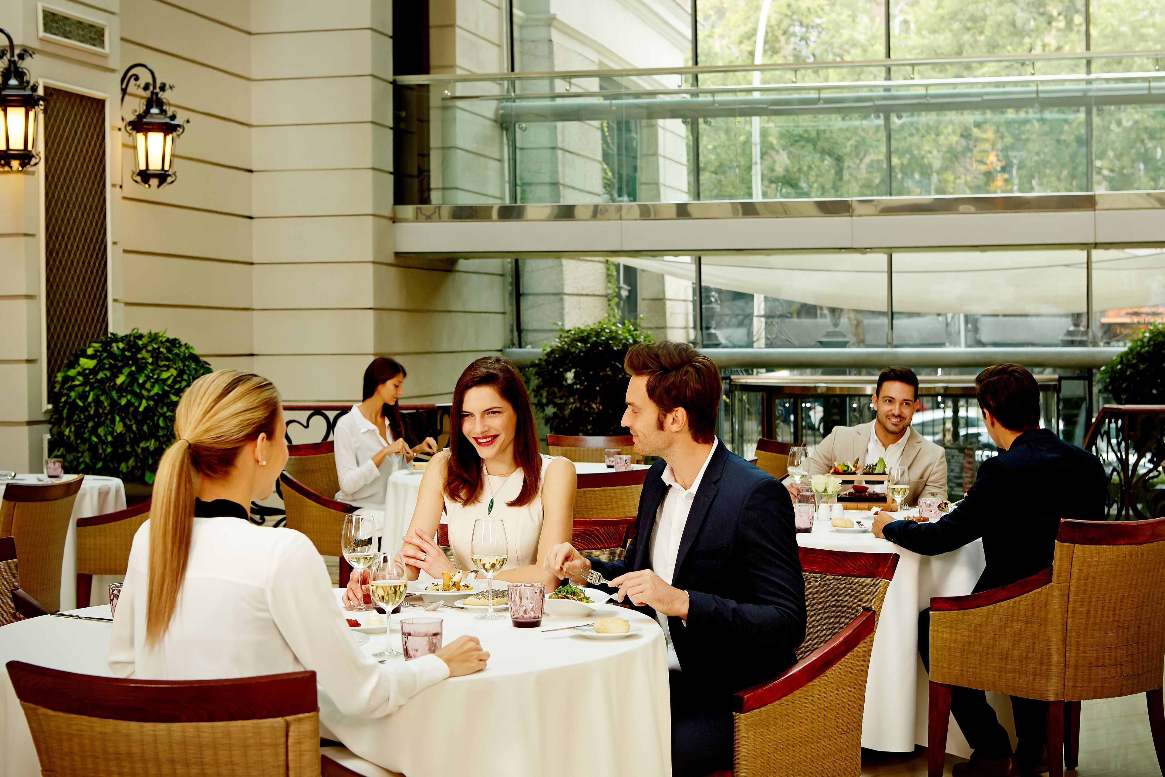 A formal dining area with round tables, wicker chairs, and a glass railing in the background.