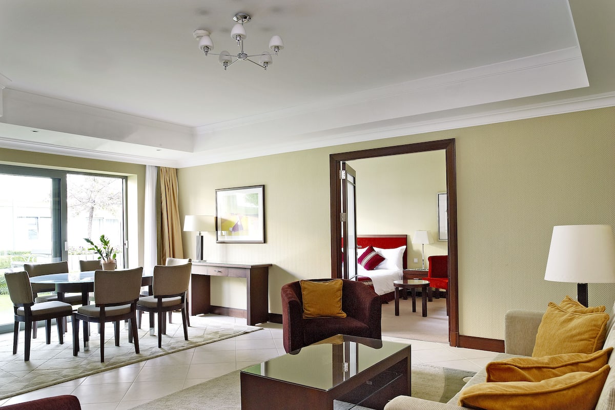 Een hotelkamer met een zithoek, een bed met rode en witte beddengoed, een rode fauteuil, een gele fauteuil en een grote spiegel.