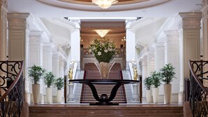 Una imponente escalera con candelabro, columnas blancas y plantas en macetas.