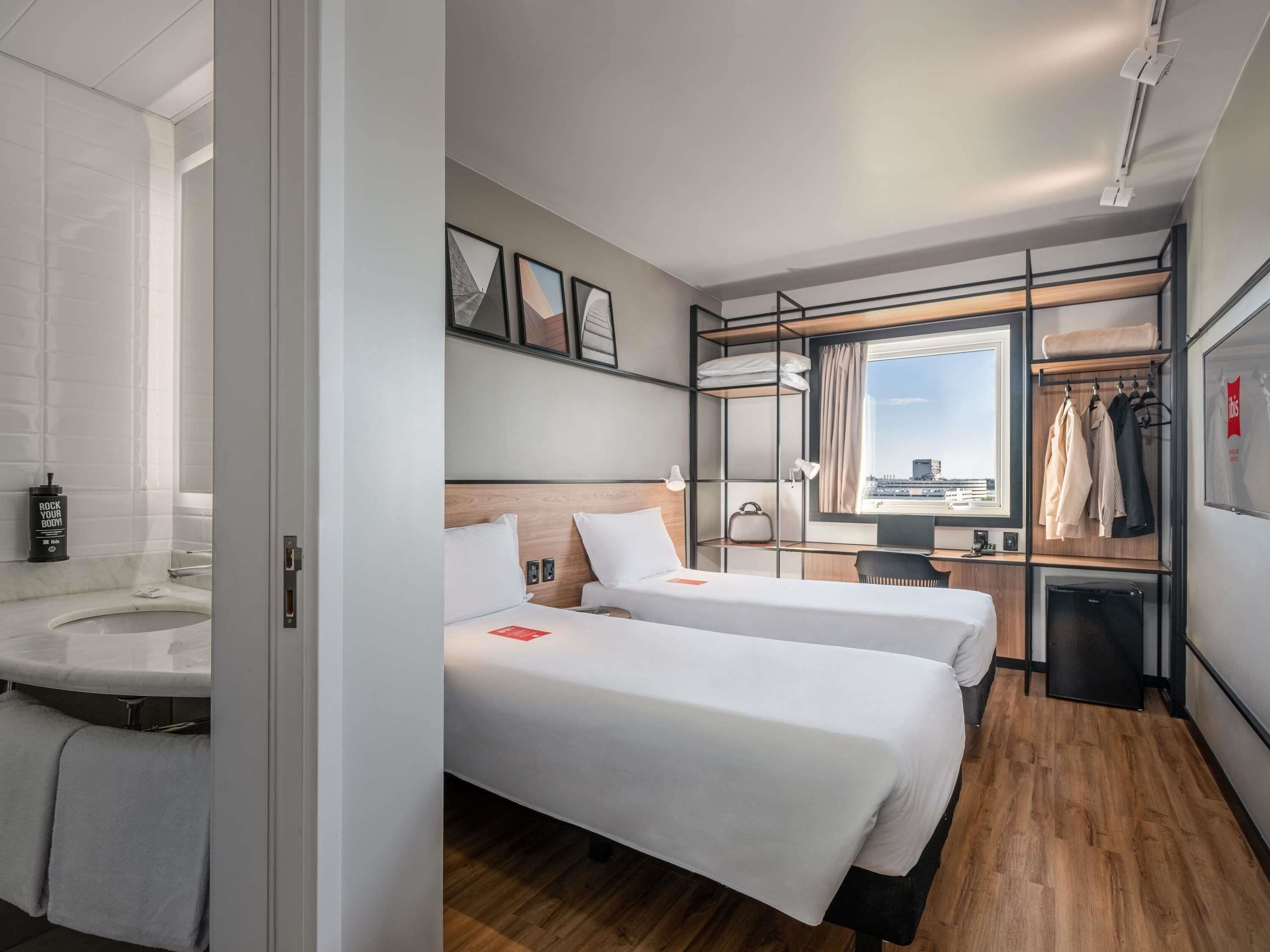 Habitación de hotel con dos camas, baño, escritorio y vista a la ciudad.